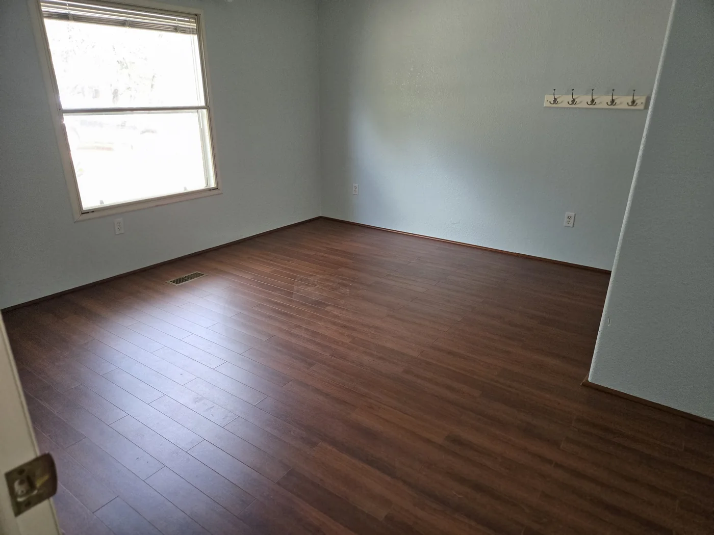 An empty room with wood flooring and pale blue walls, photographed during Diane's cleanout work